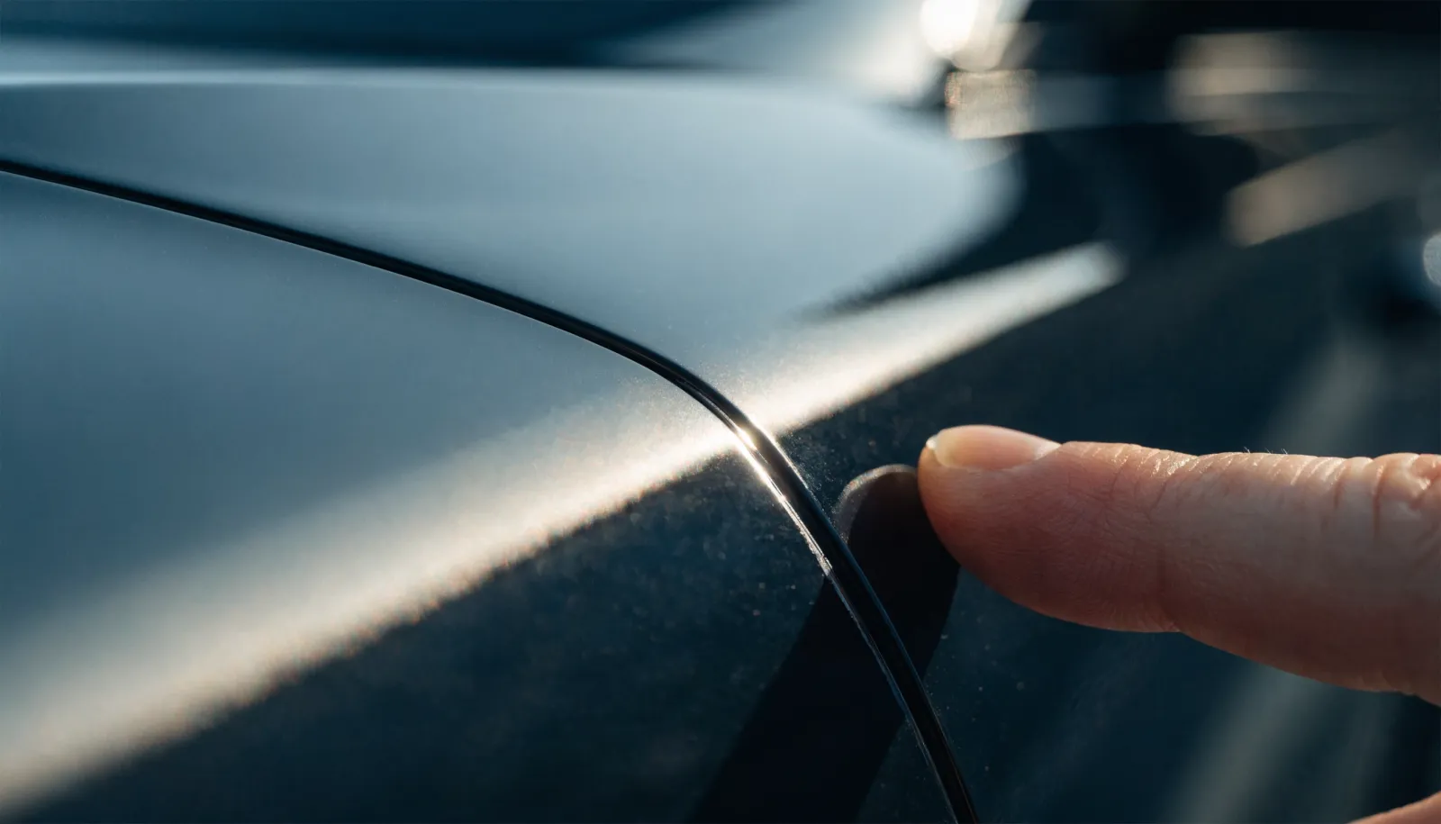 Close-up of a fingertip near a fine scratch on a glossy dark car panel