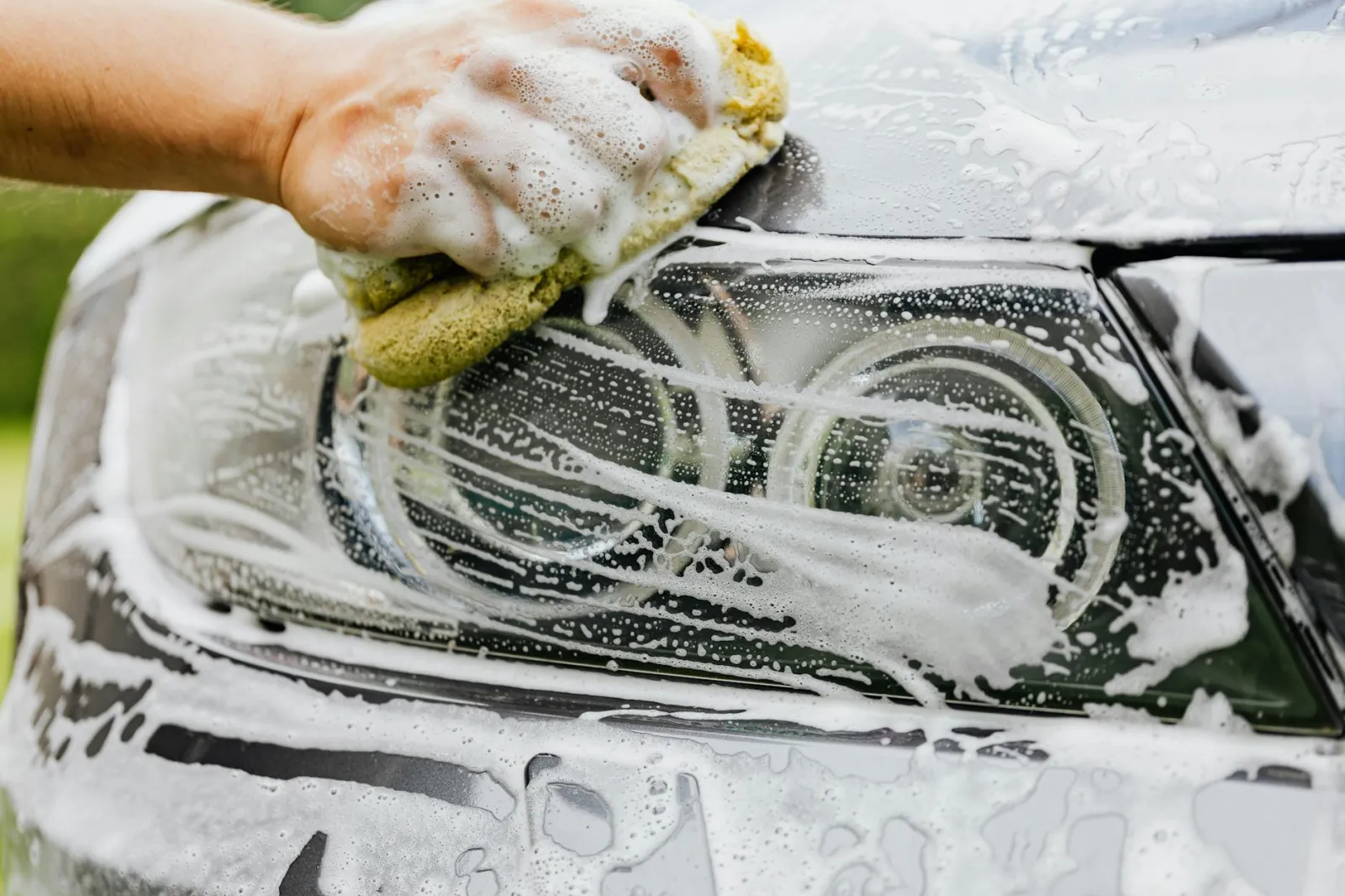 Person washing a dark car door panel with a foam-covered wash mitt