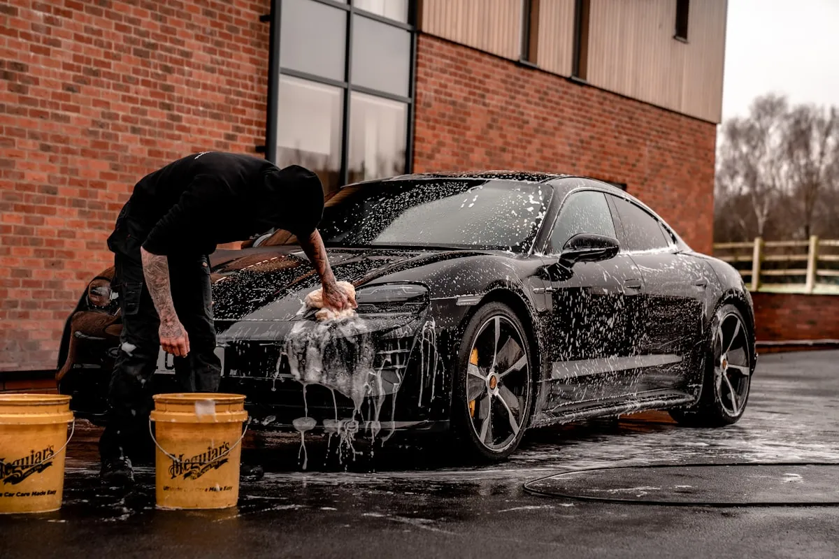 Person rinsing a dark vehicle with a pressure washer in a clean garage