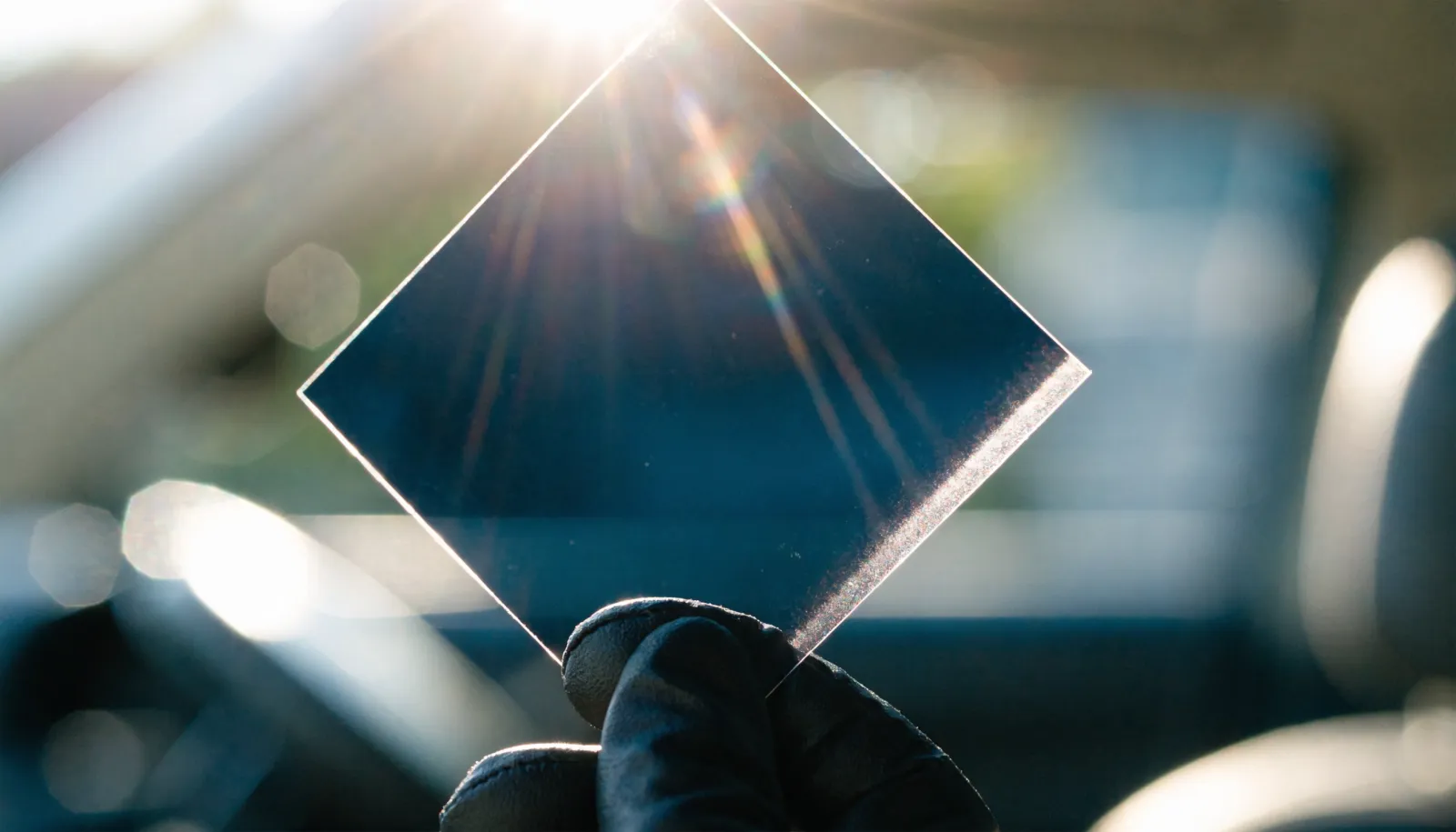 Close-up of a gloved hand holding a window film sample swatch against bright sunlight